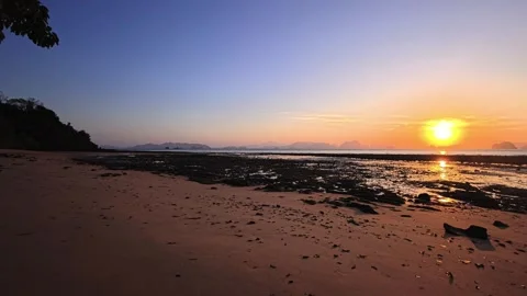 Sunset over tropical white sand beach with rocky tidal shore, wet sand and ocean Stock Footage 332212665