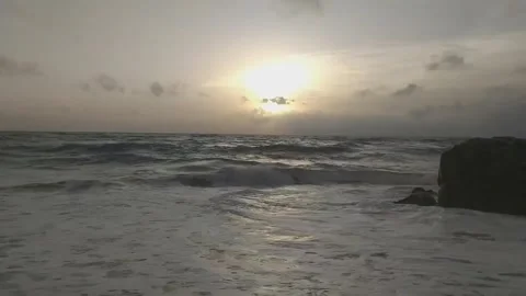 Sunset over a turbulent ocean, waves crashing on a sandy beach near dark rock Stock Footage 302308288