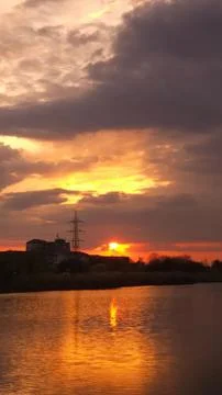 Sunset over water with clouds and reflection on calm lake Stock Photos