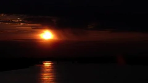 Sunset over water with dark clouds and glowing sky Stock Photos