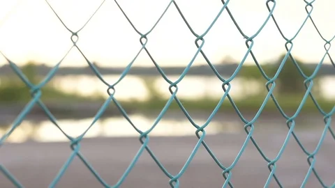 Sunset over water surface through colored green fence from the mesh Stock Footage 77576229