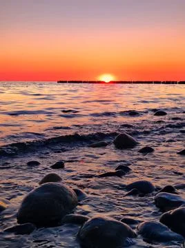Sunset over water with waves and stones along the shore in a coastal area Stock Photos