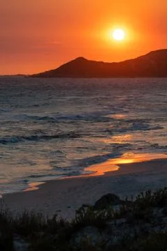 Sunset over waves on a beach with red and orange sky and yellow sun Stock Photos