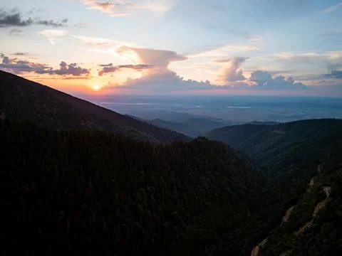 Sunset over winding road through mountain forest valley, aerial drone view Stock Photos