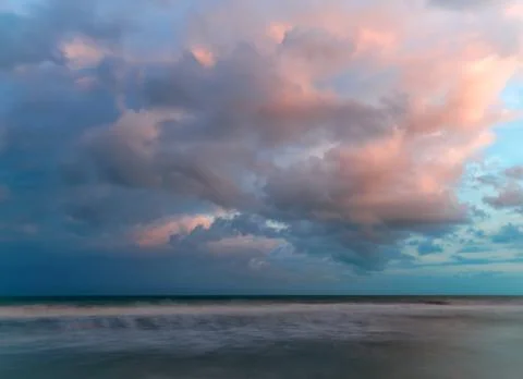 Sunset painted fluffy cloud over the soft, long exposure waves Stock Photos