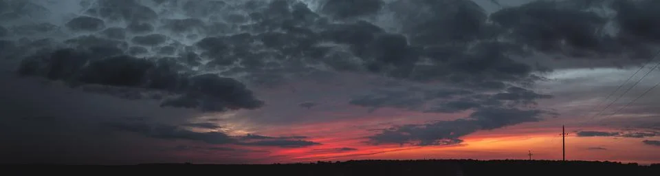 Sunset panorama with raspberry clouds over a small town against a blue sky Stock Photos