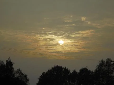 Sunset partially hidden by gray clouds above forest. Stock Photos