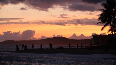Sunset with pink clouds on the beach with surfers in the ocean and tourists Vídeo Stock 104455359