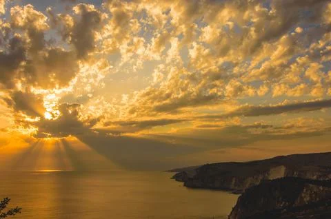 Sunset rays over sea and dramatic coastal cliffs. Stock Photos