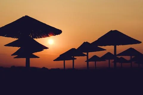 The sunset red sun illuminates the beach silhouette straw umbrellas Stock Photos