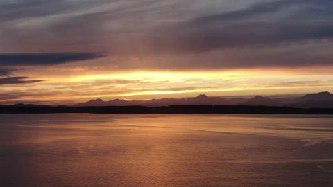 Sunset reflecting off the ocean and silhouetting a mountain range Stock Footage 169540924