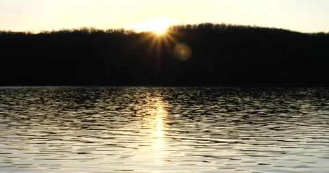 Sunset reflecting off water with forest and background establishing shot Stock Footage 234855652