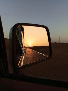 Sunset reflection in car side mirror on empty road golden hour Stock Photos