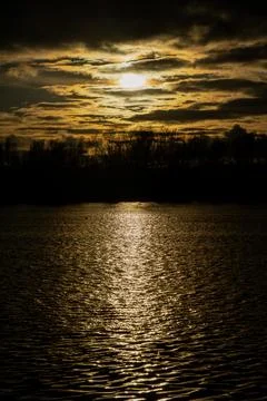 Sunset reflection on rippled river surface beneath dark clouds Stock Photos