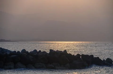 Sunset reflections over tranquil waters with rocky shoreline near distant m.. Stock Photos