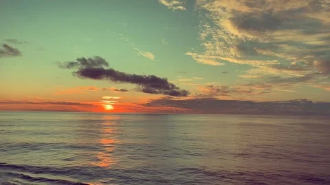 Sunset reflects vibrant colors over a tranquil ocean under a sky with scatt.. Stock Footage 338281977