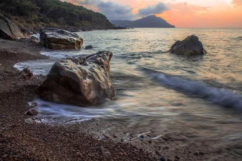Sunset of rocks beach  with orange clouds in sky and forest long expose Stock Photos