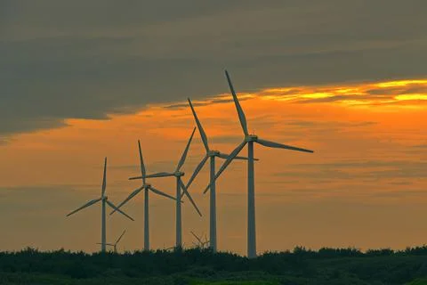 Sunset scene on the beach. Windmills in the queue. Stock Photos