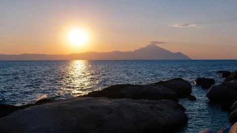 Sunset at the sea. Sun falling down behind mountain Stock Photos