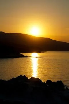 Sunset at the sea. Sun falling down behind mountain Stock Photos