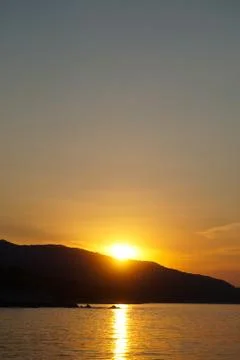 Sunset at the sea. Sun falling down behind mountain Stock Photos