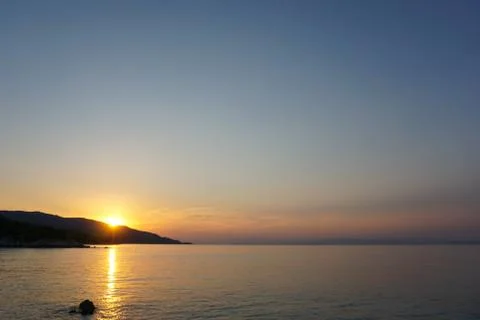 Sunset at the sea. Sun falling down behind mountain Stock Photos