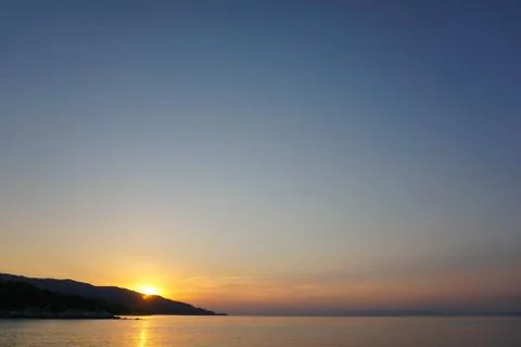 Sunset at the sea. Sun falling down behind mountain Stock Photos