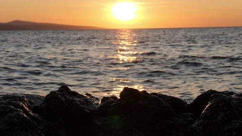 Sunset in the sea. Waves crush on black stones and splashes shine in sunlight Video stock 125640968