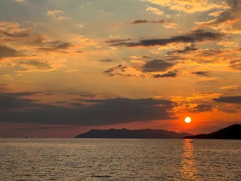 The sunset sets behind the mountains, in the foreground of the sea Stock Photos