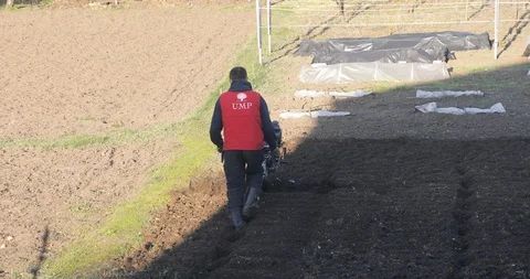 Sunset shot of farmer using the rototiller to plow the black soil. Agriculture Stock Footage 127994388