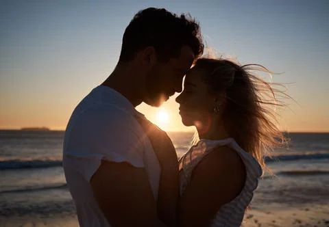 Sunset, silhouette and couple with love at the beach, affection and quality time Stock Photos