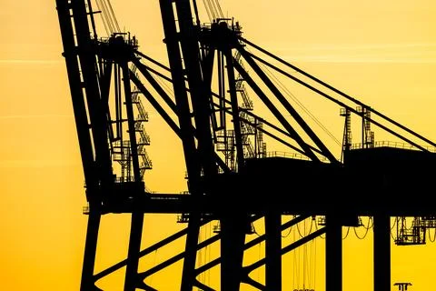 Sunset silhouette of container ship loading cranes Stock Photos