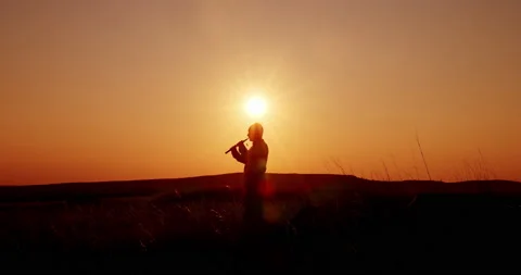 Sunset, silhouette of a man playing the pipe. Folk musician plays in the field Stock-Footage 145915165