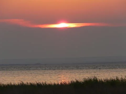 Sunset sitting between clouds on a water surface with a small ripple Stock Photos