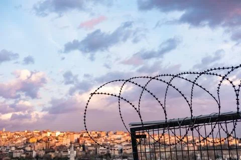 Sunset sky and barbed wire over a city. Barbed wire fence- restricted area Stock Photos