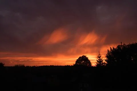Sunset sky with clouds in the form of flames. Bright orange rays illuminate Photos