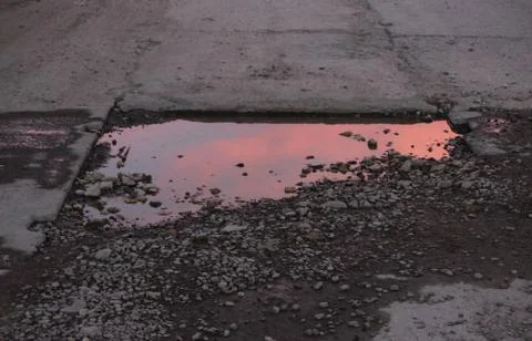 Sunset sky with clouds reflected in a puddle on a road of concrete slabs. Stock Photos