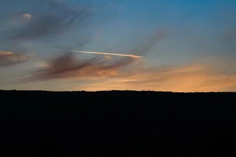 Sunset sky with contrail over dark horizon Stock Photos