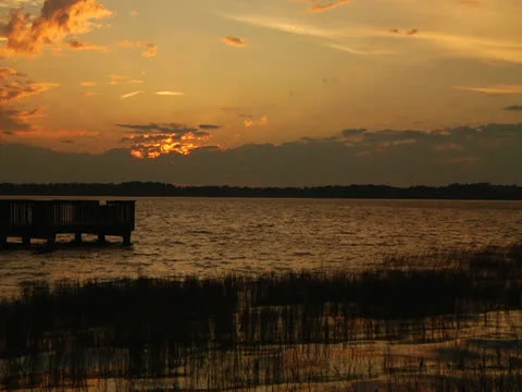 Sunset sky over lake horizon dock grass foreground wider Stock Footage