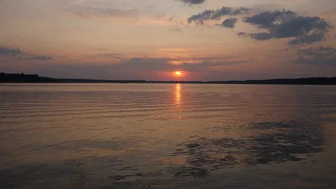 Sunset sky over rippling waters of a lake. Red sun in clouds over horizon 库存影片 121723995