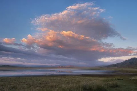 Sunset sky with pink clouds reflecting in the calm waters of Lake Tuzkol surr Stock Photos