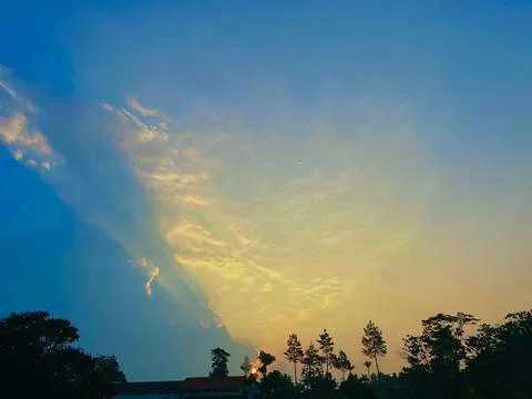 Sunset Sky with Sun Rays Piercing Through the Clouds Above Tree Silhouettes Stock Photos