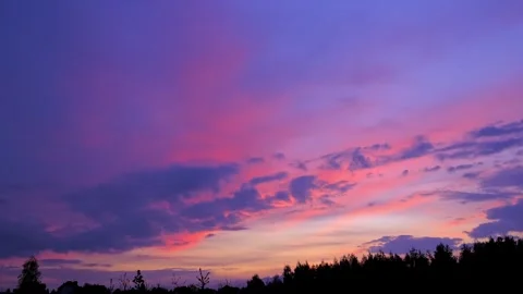 Sunset sky with vibrant pink and purple clouds over a dark forest silhouette Stock Footage 344883242