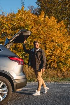 At sunset, a smiling man closes the trunk of a parked car Stock Photos