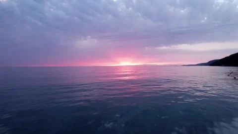 Sunset Spreading Vibrant Colors over Calm Clear Waters with Dramatic Clouds Stock Footage 320799426