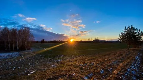 Sunset in the spring evening with a green meadow and birch trees with a blue Stock Photos