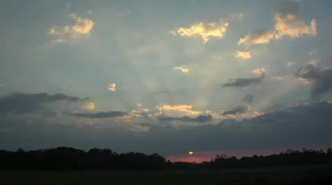 Sunset streaks behind dark and gold clouds over low treeline time lapse Stock Footage 10830058