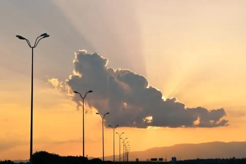 Sunset with sun behind cloud. Orange sun rays on highway Stock Photos