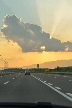 Sunset with sun behind cloud. Orange sun rays on highway Stock Photos