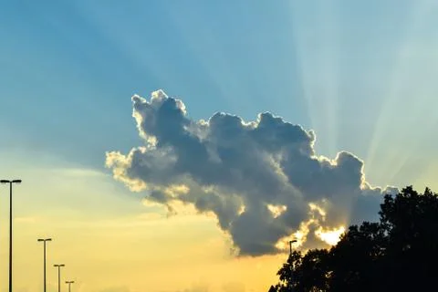 Sunset with sun behind cloud. Yellow sun rays with blue sky Stock Photos